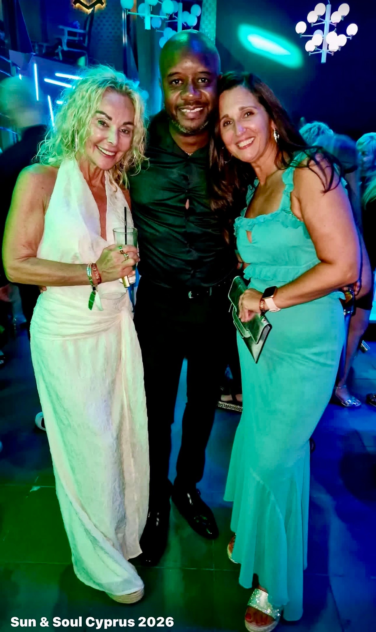 Three friends smiling together under teal lights at Sun & Soul Cyprus 2026